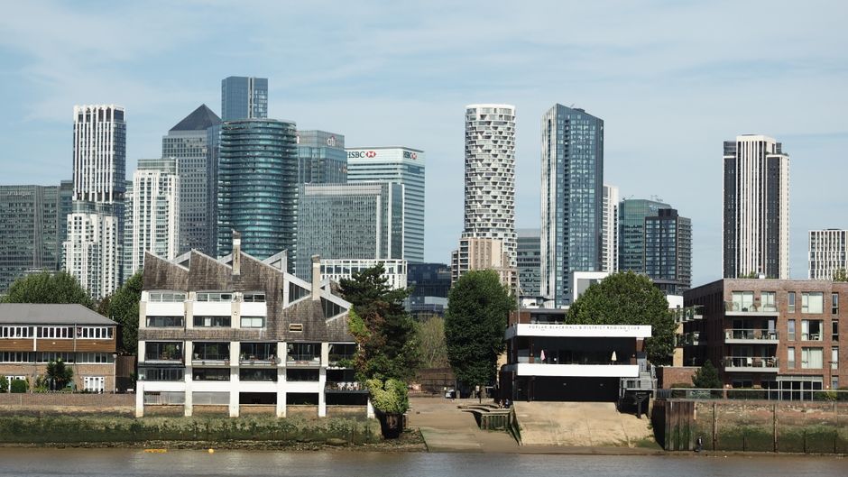A scenic view of Thames View Estate Creekmouth featuring modern high-rise office buildings and residential apartments in the background, with a few lower-rise older residential buildings and lush gree